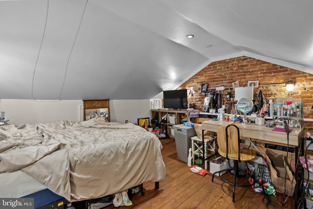 bedroom with wood-type flooring, vaulted ceiling, and brick wall