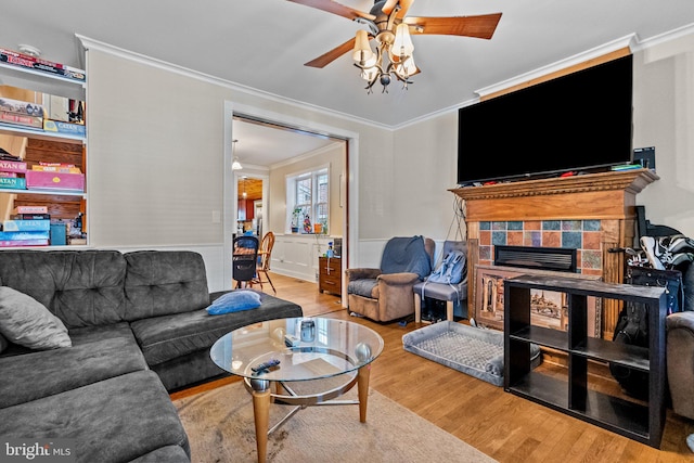 living room featuring ceiling fan, crown molding, light wood-type flooring, and a fireplace