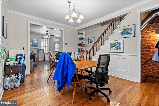 home office with ornamental molding, brick wall, ceiling fan with notable chandelier, and light hardwood / wood-style floors