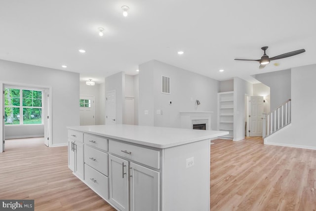 kitchen with white cabinets, ceiling fan, a center island, and light hardwood / wood-style floors