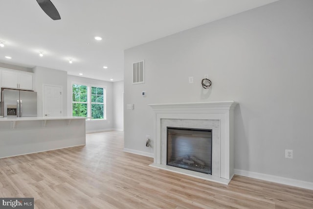 unfurnished living room with ceiling fan, light hardwood / wood-style flooring, and a high end fireplace