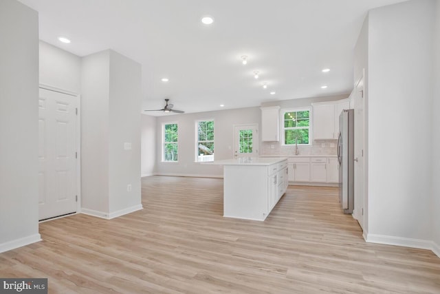 kitchen featuring a center island, white cabinets, light hardwood / wood-style flooring, ceiling fan, and stainless steel refrigerator