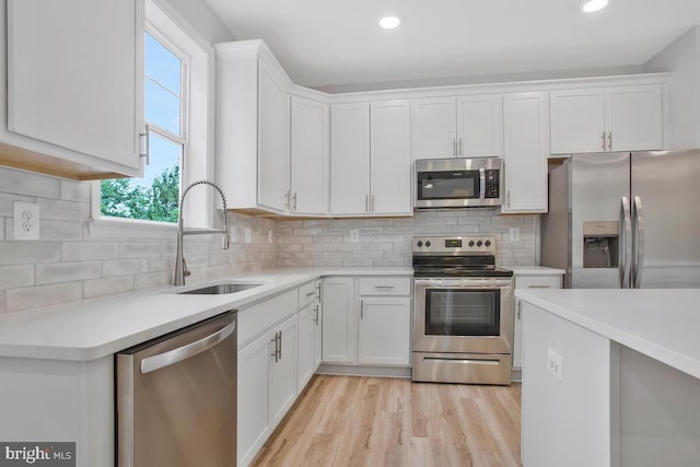 kitchen with appliances with stainless steel finishes, light wood-type flooring, tasteful backsplash, sink, and white cabinets