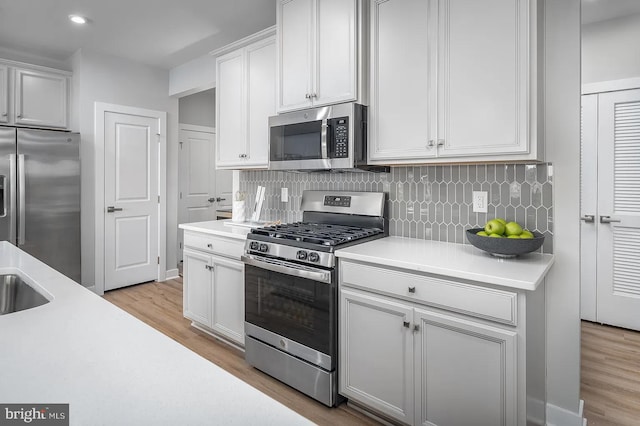 kitchen with decorative backsplash, white cabinetry, stainless steel appliances, and light wood-type flooring