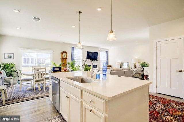 kitchen featuring dishwasher, sink, light hardwood / wood-style flooring, decorative light fixtures, and a center island with sink