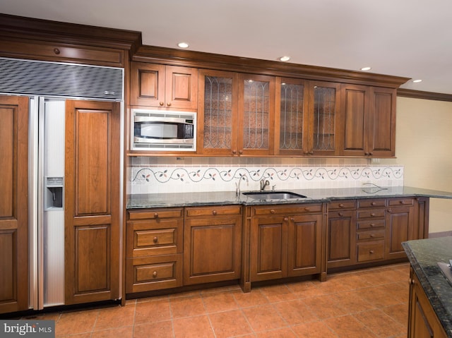 kitchen with dark stone counters, sink, built in appliances, decorative backsplash, and light tile patterned floors