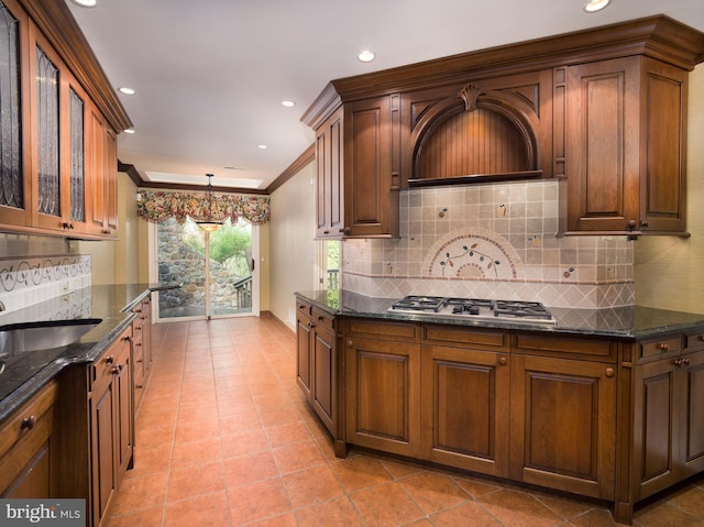 kitchen with backsplash, dark stone counters, stainless steel gas cooktop, crown molding, and a chandelier