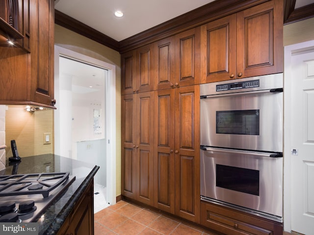 kitchen featuring appliances with stainless steel finishes, light tile patterned floors, crown molding, and dark stone countertops