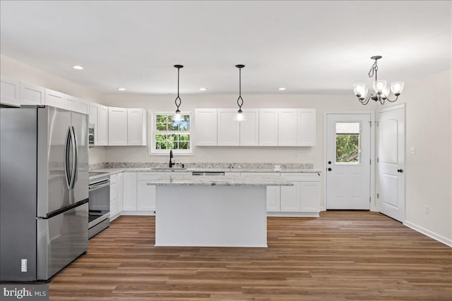 kitchen with white cabinetry, sink, stainless steel appliances, decorative light fixtures, and a kitchen island