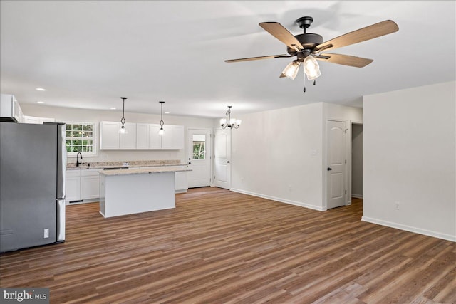 kitchen featuring stainless steel fridge, ceiling fan with notable chandelier, white cabinets, a center island, and hanging light fixtures