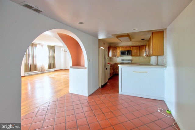 kitchen with backsplash, a baseboard heating unit, stainless steel stove, light wood-type flooring, and white fridge