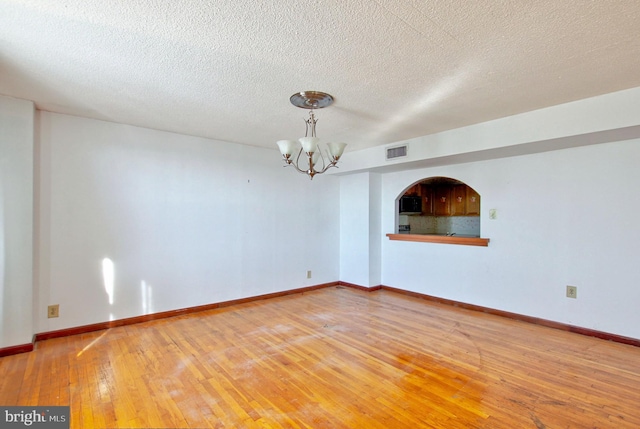 unfurnished room featuring hardwood / wood-style floors, a notable chandelier, and a textured ceiling