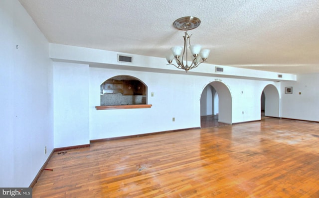 spare room featuring a chandelier, wood-type flooring, and a textured ceiling