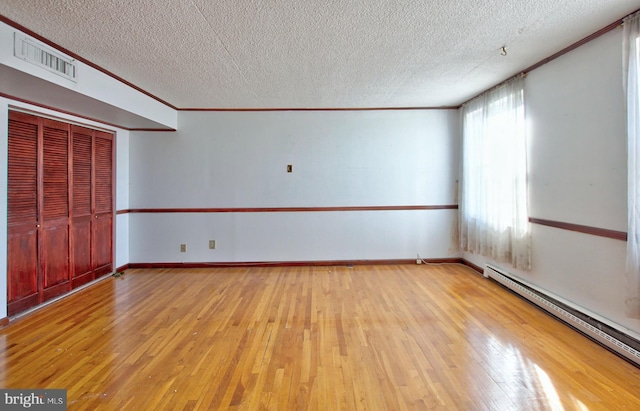 spare room featuring baseboard heating, crown molding, light hardwood / wood-style flooring, and a textured ceiling