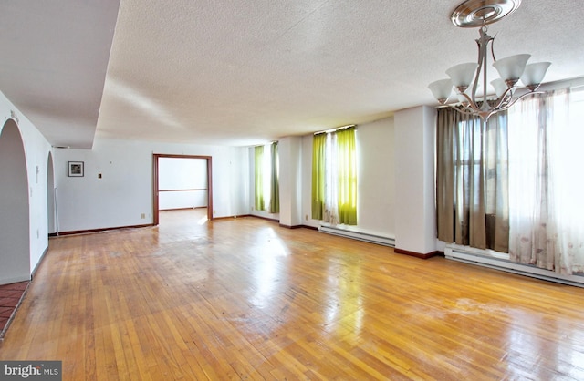 spare room with a notable chandelier, a healthy amount of sunlight, light wood-type flooring, and a baseboard radiator