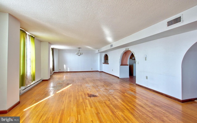 spare room featuring a chandelier, a baseboard radiator, a textured ceiling, and wood-type flooring