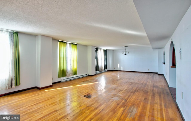 spare room featuring hardwood / wood-style floors, a baseboard radiator, a healthy amount of sunlight, and a notable chandelier