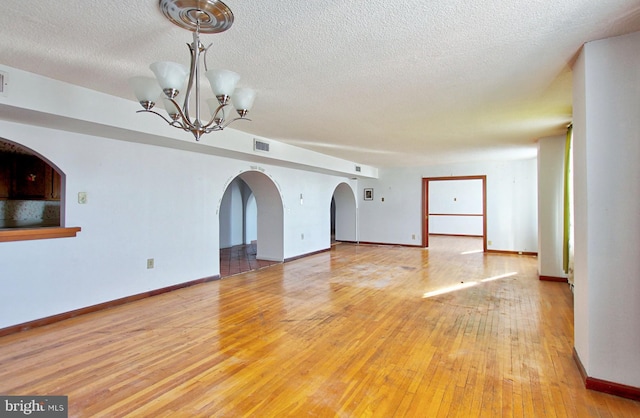 empty room featuring light hardwood / wood-style flooring, a chandelier, and a textured ceiling