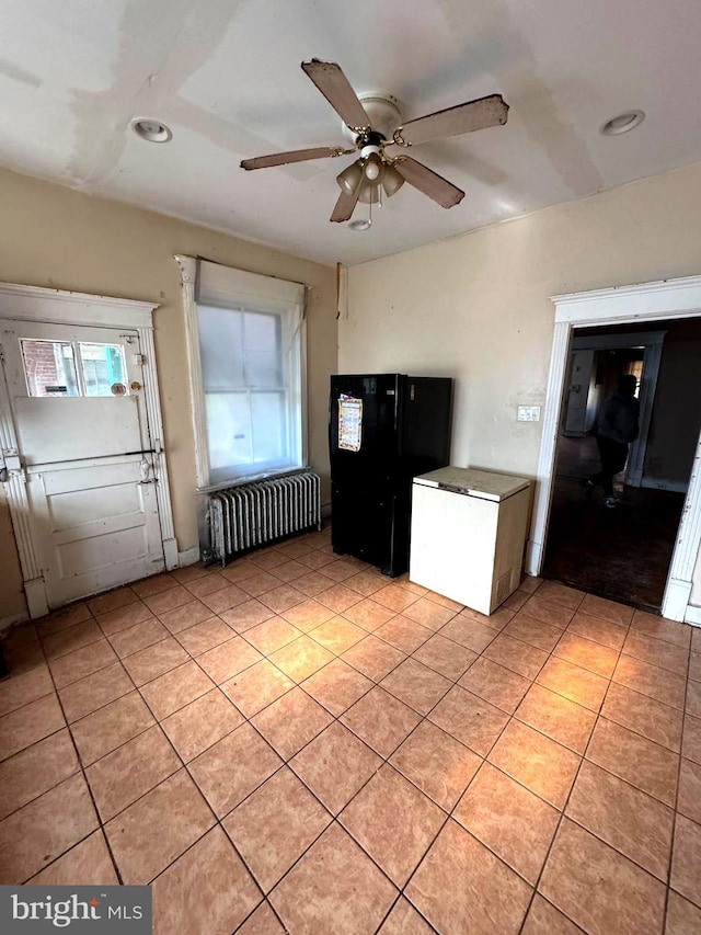 kitchen featuring radiator, black fridge, ceiling fan, and light tile patterned flooring