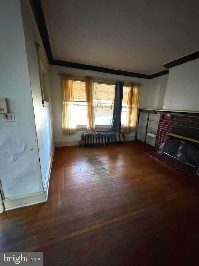 unfurnished living room featuring a fireplace, ornamental molding, dark wood-type flooring, and radiator