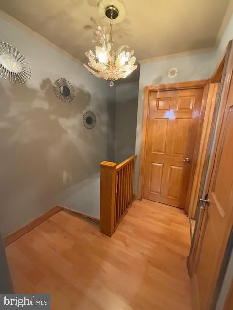 hall with crown molding, light hardwood / wood-style floors, and an inviting chandelier