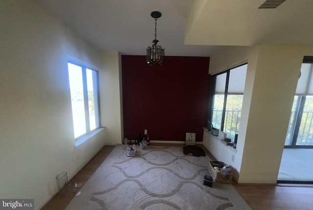 unfurnished dining area featuring wood-type flooring, a healthy amount of sunlight, and an inviting chandelier