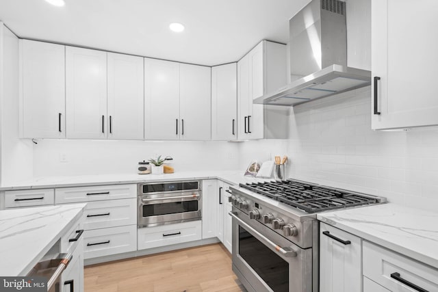 kitchen featuring white cabinets, wall chimney range hood, and appliances with stainless steel finishes