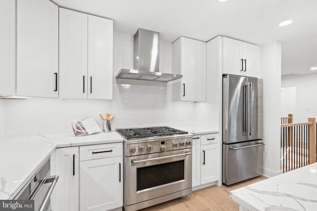 kitchen with decorative backsplash, light wood-type flooring, premium appliances, wall chimney range hood, and white cabinets