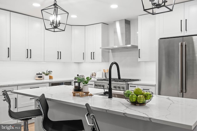 kitchen featuring white cabinets, stainless steel appliances, a kitchen island with sink, and wall chimney range hood