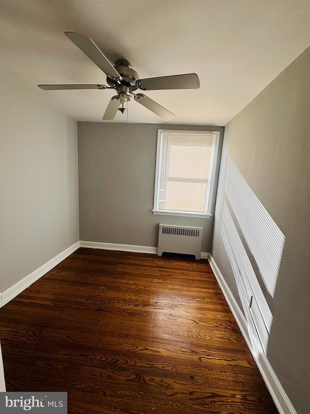 empty room with ceiling fan, dark hardwood / wood-style flooring, and radiator heating unit