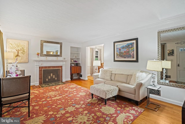 living room featuring built in shelves, hardwood / wood-style flooring, a brick fireplace, and crown molding