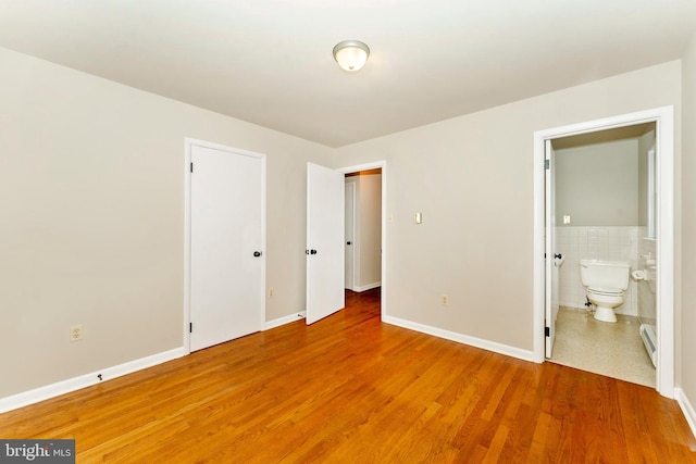 unfurnished bedroom featuring a baseboard heating unit, ensuite bath, hardwood / wood-style flooring, tile walls, and a closet