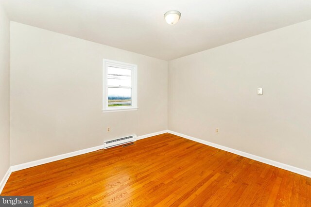 empty room featuring hardwood / wood-style floors and a baseboard heating unit