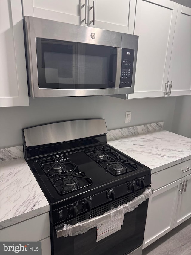 kitchen with light stone countertops, white cabinets, stainless steel appliances, and hardwood / wood-style flooring