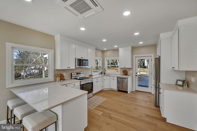 kitchen featuring kitchen peninsula, a kitchen breakfast bar, stainless steel appliances, a healthy amount of sunlight, and white cabinets