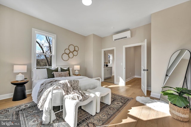 bedroom featuring a wall mounted air conditioner, light hardwood / wood-style floors, and connected bathroom