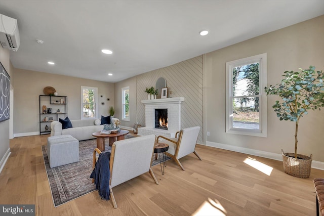 living room featuring an AC wall unit, plenty of natural light, light hardwood / wood-style floors, and a brick fireplace