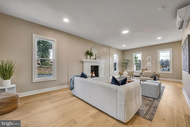 living room featuring a wall mounted air conditioner, light hardwood / wood-style floors, and a brick fireplace