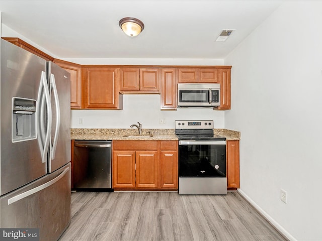 kitchen with light stone counters, sink, light hardwood / wood-style floors, and appliances with stainless steel finishes