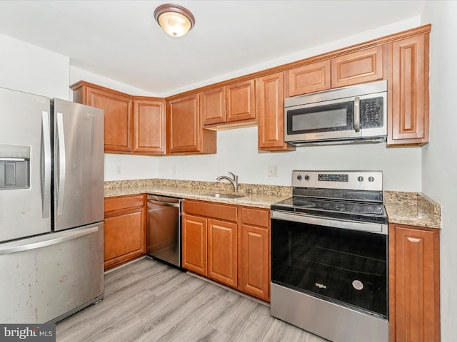 kitchen with light stone counters, sink, light wood-type flooring, and appliances with stainless steel finishes