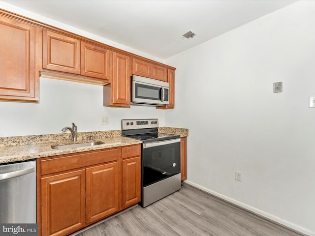 kitchen with light stone counters, sink, stainless steel appliances, and light hardwood / wood-style flooring