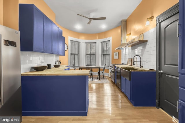 kitchen featuring blue cabinetry, butcher block counters, ceiling fan, appliances with stainless steel finishes, and light wood-type flooring