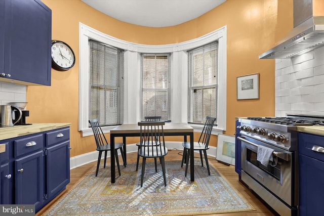 kitchen with blue cabinetry, decorative backsplash, wall chimney range hood, and high end stainless steel range oven