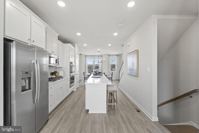 kitchen with white cabinetry, a center island, stainless steel appliances, decorative light fixtures, and a breakfast bar area