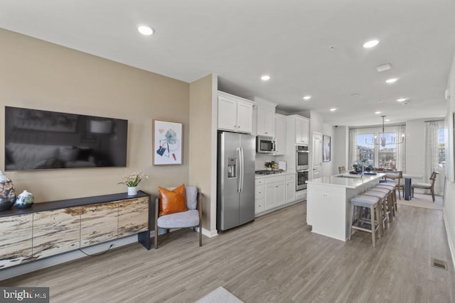 kitchen with a breakfast bar, stainless steel appliances, white cabinetry, and a center island with sink