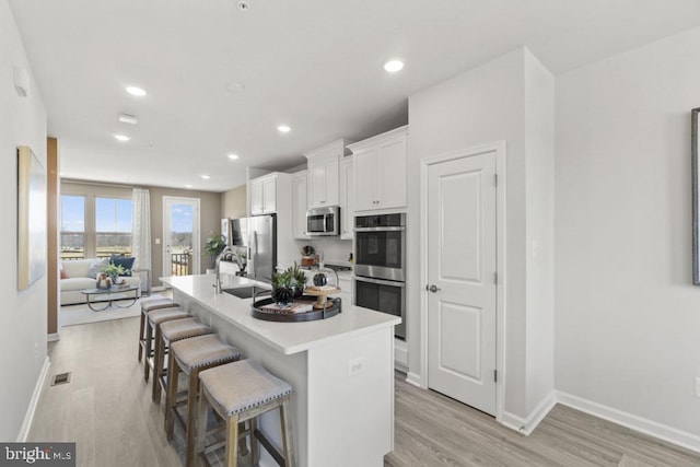 kitchen with stainless steel appliances, light hardwood / wood-style flooring, a breakfast bar, white cabinets, and a center island with sink