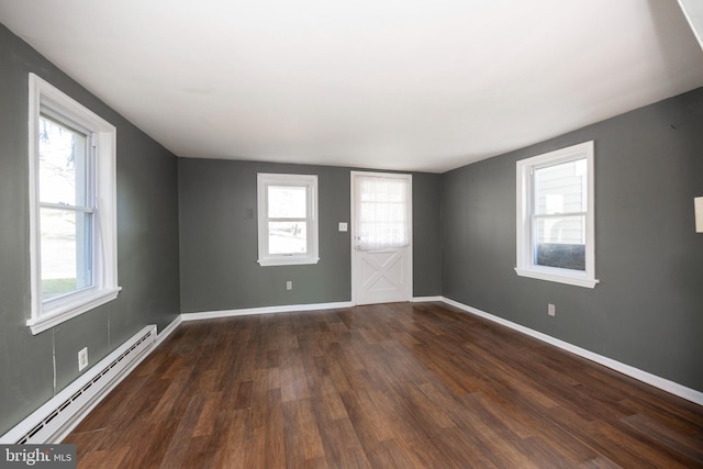 empty room featuring baseboard heating, a wealth of natural light, and dark wood-type flooring