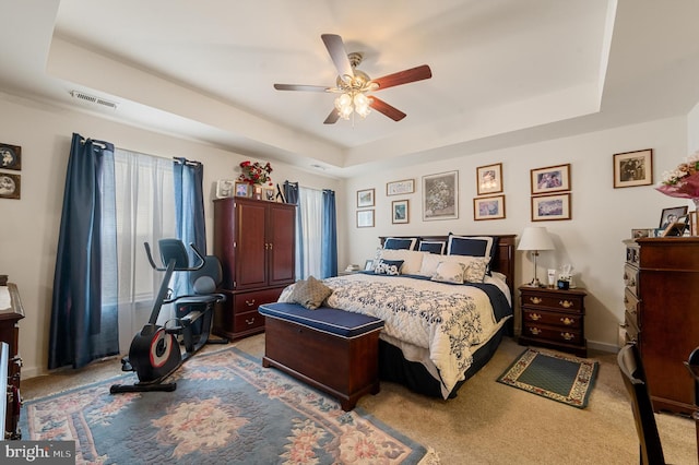 carpeted bedroom with a raised ceiling and ceiling fan