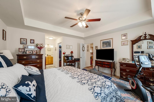 bedroom with ceiling fan, a tray ceiling, and ensuite bath