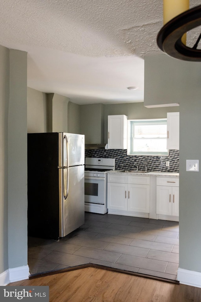 kitchen featuring white cabinets, hardwood / wood-style flooring, a textured ceiling, white range with gas stovetop, and stainless steel refrigerator